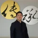 Raffles Family Office CEO Chi-Man Kwan standing in front of decorative calligraphy art
